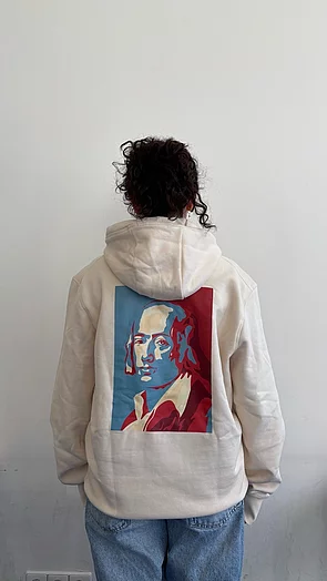 Eine Person trägt einen beigen Hoodie mit einem farbigen Porträt auf dem Rücken.