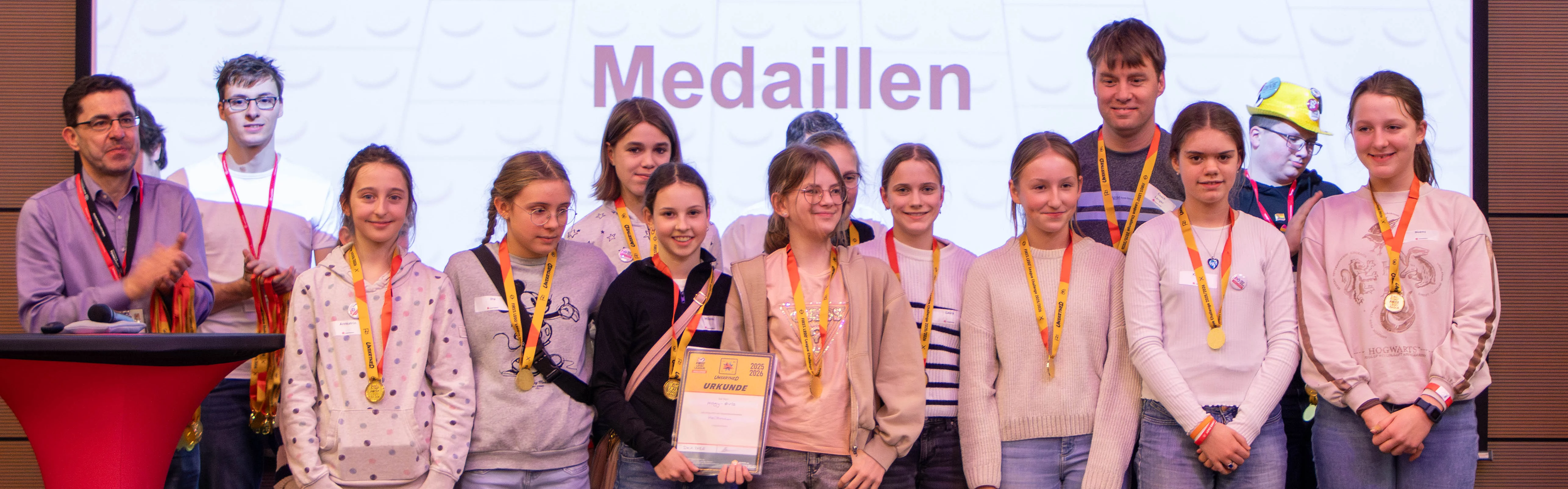 Gruppens Foto von Teilnehmern einer Lego-Wettbewerb-Veranstaltung, die Medaillen und Auszeichnungen erhalten.