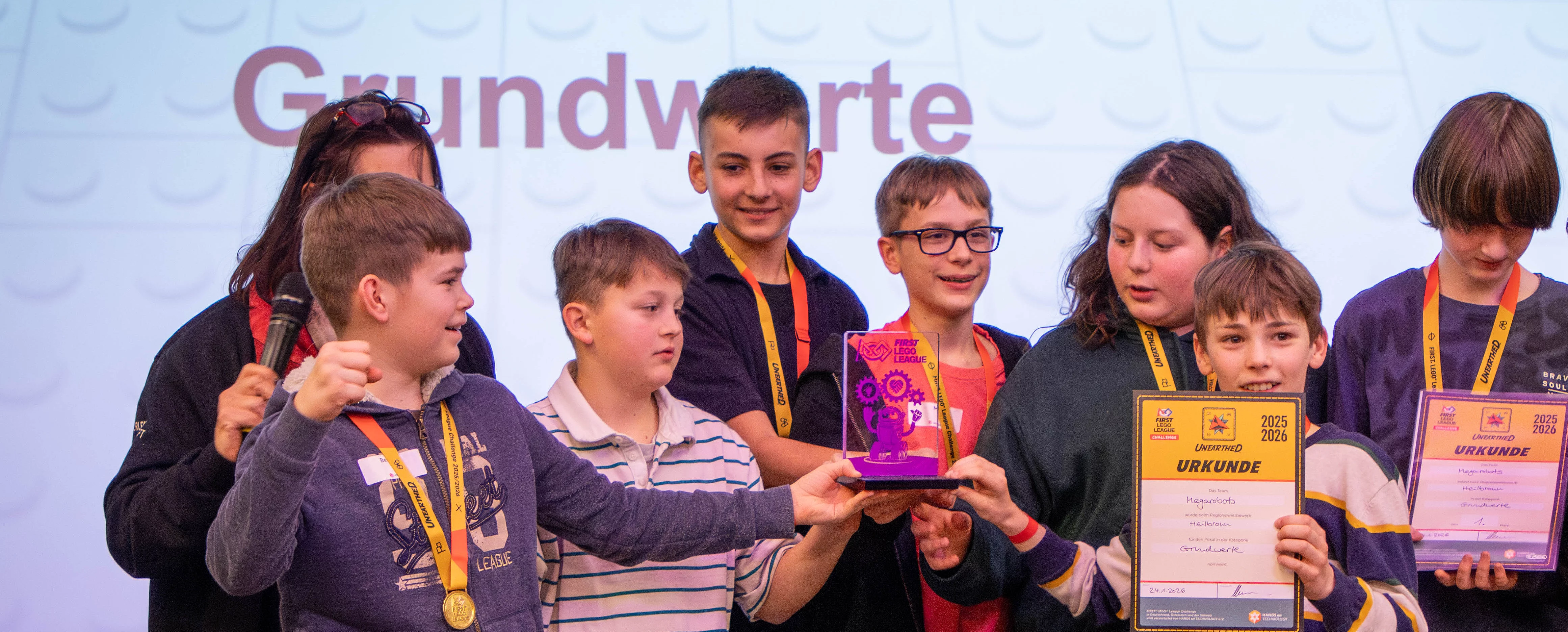 Eine Gruppe von Kindern hält Pokale und Urkunden bei einer Preisverleihung, stolz lächelnd.