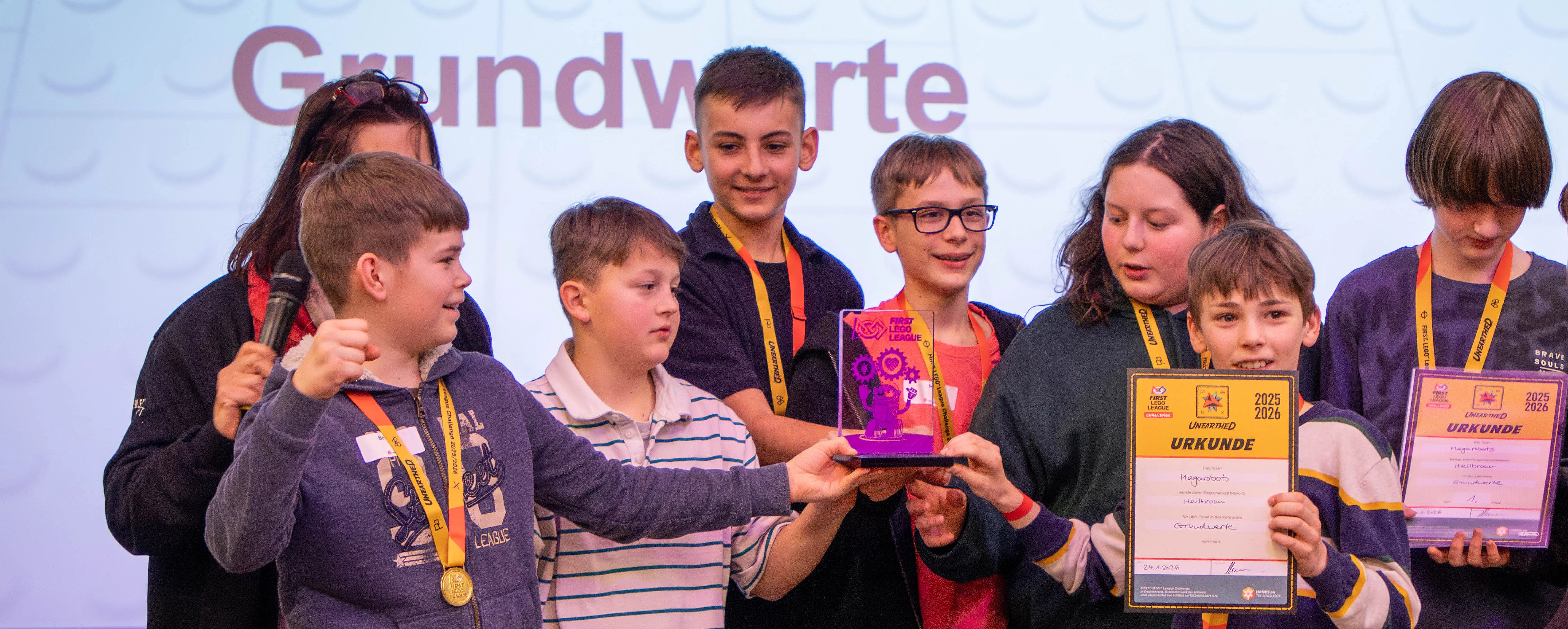 Eine Gruppe von Kindern hält Pokale und Urkunden bei einer Preisverleihung, stolz lächelnd.