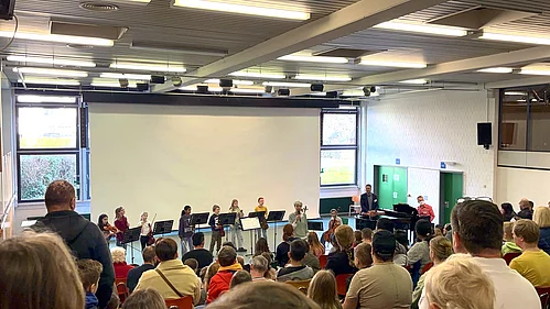 Ein Musikauftritt von Kindern mit verschiedenen Instrumenten in einem Saal vor begeistertem Publikum.