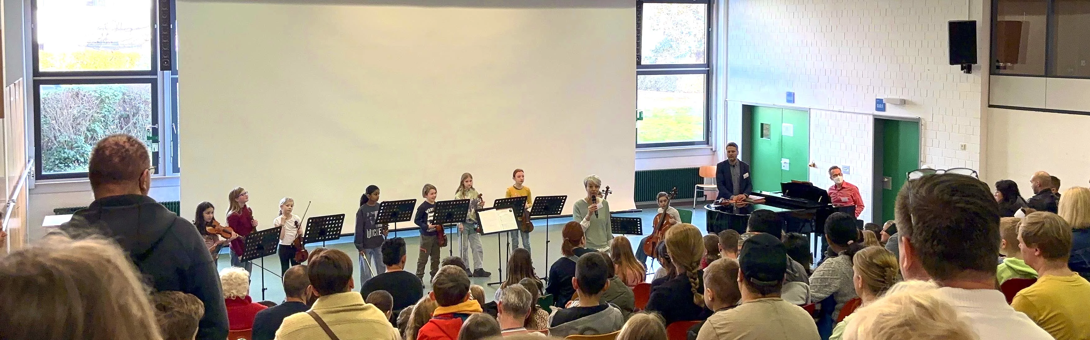 Ein Musikauftritt von Kindern mit verschiedenen Instrumenten in einem Saal vor begeistertem Publikum.