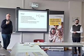 Zwei Dozenten präsentieren einen Ablaufplan für ein Unternehmensprojekt im Klassenzimmer.